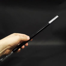Hand holding a black and silver rod against a dark background
