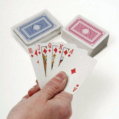 Hand holding playing cards with two decks of cards in the background on a white surface