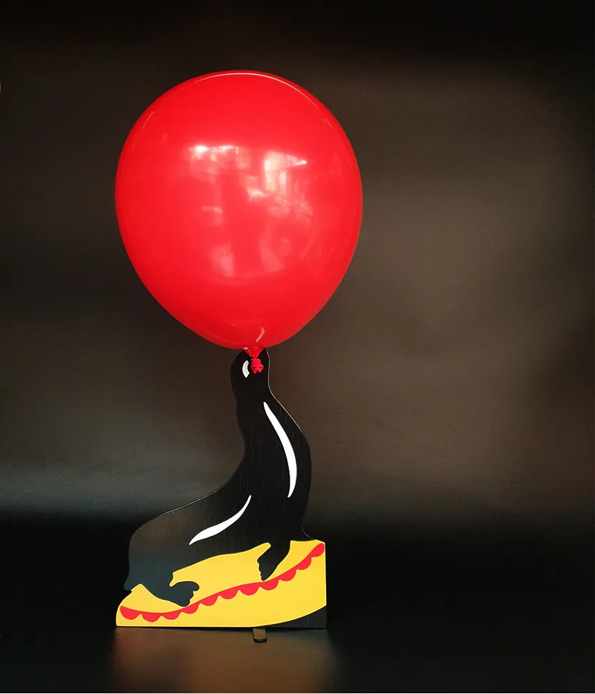Black seal figurine with a red balloon on a dark background