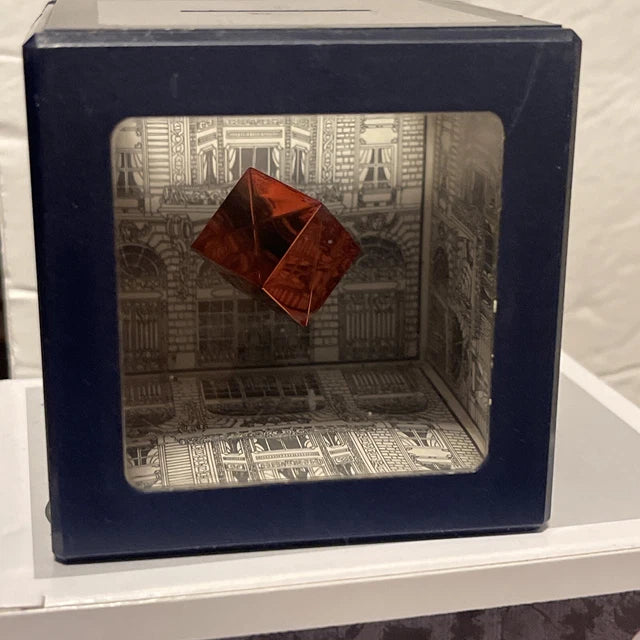 Red geometric sculpture inside a decorative box with architectural design