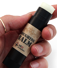 Hand holding a stick of 'Coughing Balm' with a white background