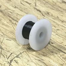 Spool of black thread on a white spool with a wooden surface background
