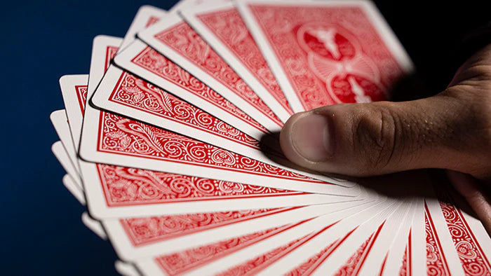 Hand holding a fan of red playing cards against a dark background