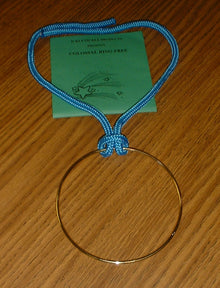 Gold ring on a blue cord with a green card underneath on a wooden surface