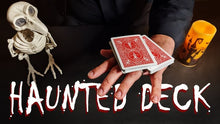 Hand holding red playing cards with a skeleton and candle on a dark background, featuring 'Haunted Deck' text.