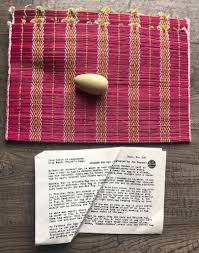 Pink woven mat with a small object on top and a piece of paper with text underneath