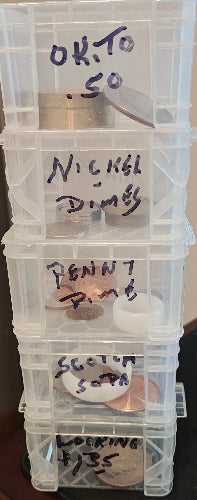 Stack of clear plastic storage bins labeled with items inside, on a wooden surface.