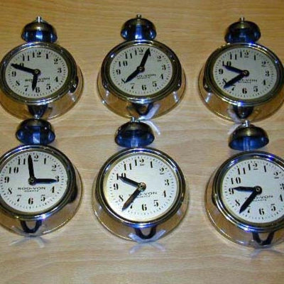 Set of six pocket watches with white faces and black hands on a wooden surface.