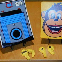 Toy camera and monkey face card on a wooden surface with scattered letters.