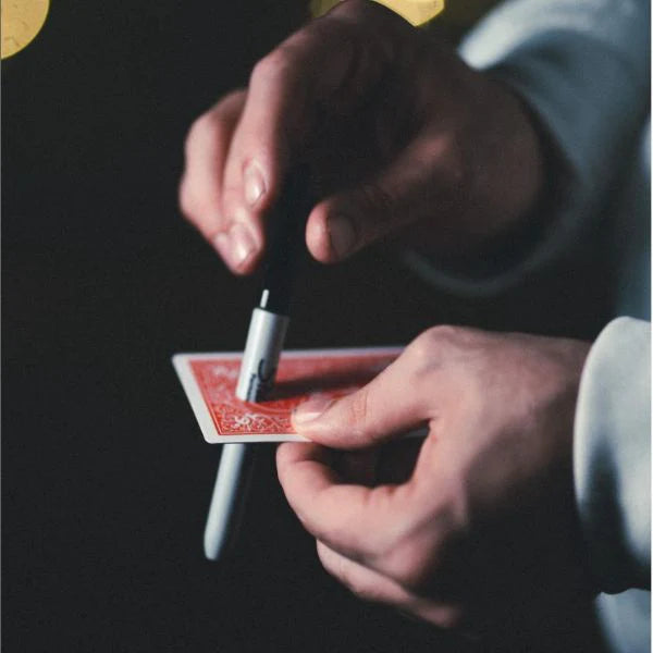 Close-up of hands performing a card trick with a pen on a dark background