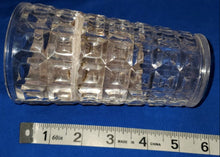 Clear glass cylindrical object with textured surface on a blue background with a ruler for scale.