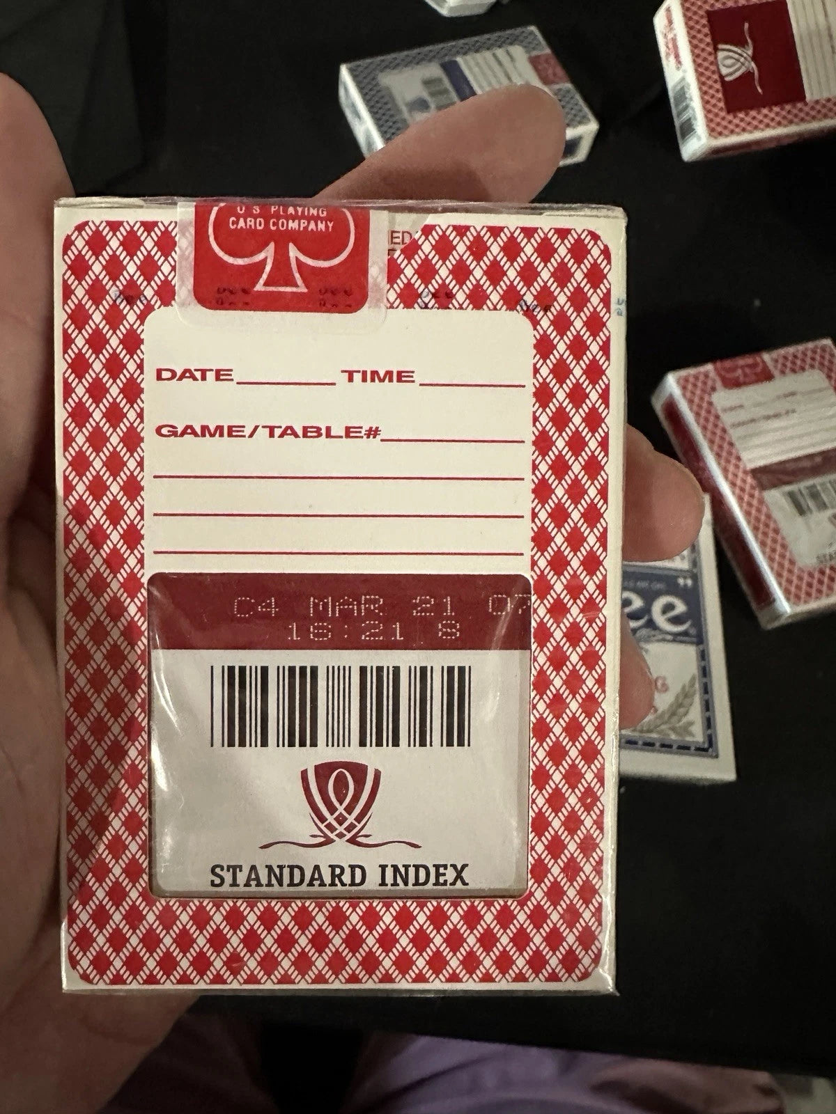 Red and white playing card box with label and barcode held by a hand.