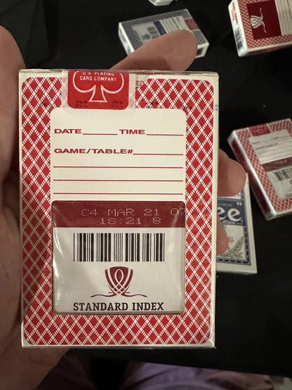 Red and white playing card box with label and barcode held by a hand.