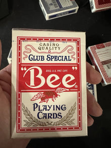 Box of Bee Club Special playing cards held by a hand on a dark background
