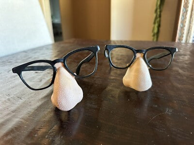 Black-framed eyeglasses on a wooden surface with two small white objects.