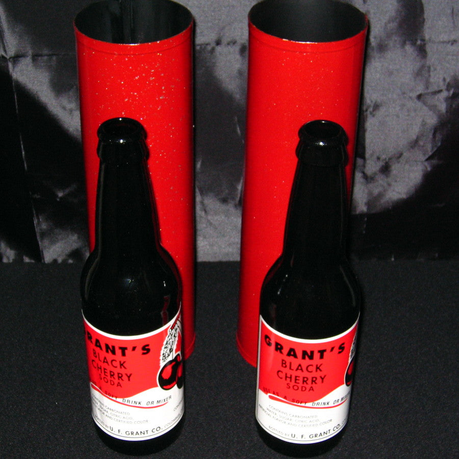 Two bottles of Grant's Black Cherry Soda with red labels and red cardboard stands on a dark surface.